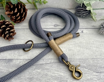May include: A gray rope leash featuring a coiled design with metallic bronze-toned hardware. The leash includes a sturdy swivel snap hook and a decorative wrapped handle section, providing a secure grip for pet walking and training activities.