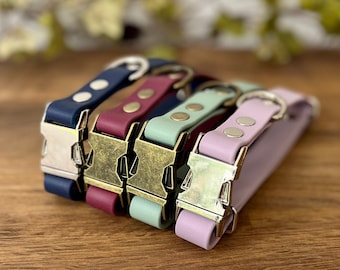 May include: Four pet collars in navy blue, deep magenta, mint green, and light lavender. Each collar features a smooth, matte-finish strap, two silver-toned rivets, a metal D-ring, and a side-release buckle in either polished silver or antique brass.