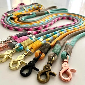 May include: A collection of multi-coloured rope leads featuring various patterns including solid, speckled, and ombre designs. Each lead is finished with a secure metal swivel snap hook in finishes such as gold, rose gold, black, and antique brass.