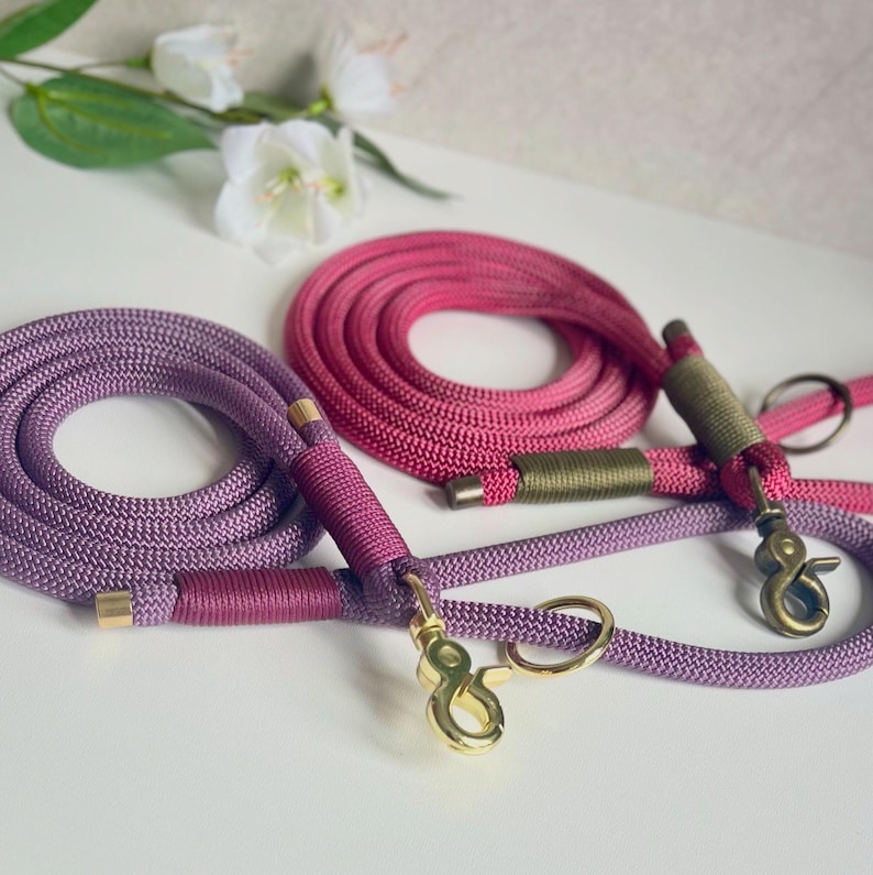 May include: Two coiled rope leashes for pets. One leash is lavender with gold-toned metal hardware and dark pink cord wrapping. The other leash is magenta with olive green cord wrapping and antique brass-toned metal hardware.