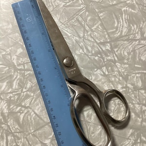May include: Silver fabric shears with a blue ruler measuring 28 inches. The shears have a pointed tip and a rounded handle.