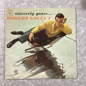 May include: A vintage vinyl record album cover featuring a man in a yellow sweater and black pants sitting in a chair. The album cover is titled "sincerely yours... ROBERT GOULET".