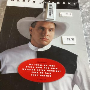 May include: Album cover for Garth Brooks, featuring a man in a cowboy hat. The cover is black and white with a red oval sticker listing song titles. A price tag is visible.