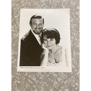 May include: Black and white photograph of a smiling man and woman. The man wears a suit and tie, and the woman is in a dress. The text "EARL WRIGHTSON and LOIS HUNT" is printed at the bottom of the photo.