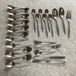 May include: A set of stainless steel silverware with an ornate design. The set includes spoons, forks, and a serving spoon.