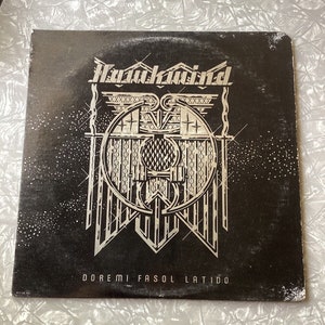 May include: Black vinyl record with a silver and white graphic design of a stylized letter "R" with wings and a circle around it. The text "Hawkwind" is at the top of the record and "DOREMI FASOL LATIDO" is at the bottom.