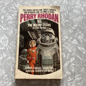 May include: Vintage paperback book titled "Perry Rhodan 55: The Micro-Techs" by Clark Darlton. The cover art features a retro sci-fi illustration of a man in an orange suit and a large robot. The book's title and author are prominently displayed.
