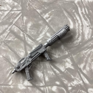 May include: A silver toy gun with a futuristic design. The gun has a barrel with a series of ridges and a handle with a trigger.