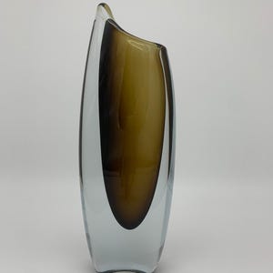 May include: A clear glass vase with a brown and yellow swirl design. The vase is tall and slender with a rounded bottom.