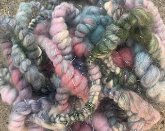 May include: A skein of hand-dyed yarn in shades of pink, teal, green, and gray with silver metallic thread woven throughout.