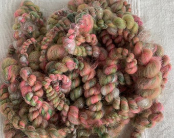 May include: A close-up of a ball of yarn with pink, green, and silver threads. The yarn is soft and fluffy, and it would be perfect for knitting or crocheting.