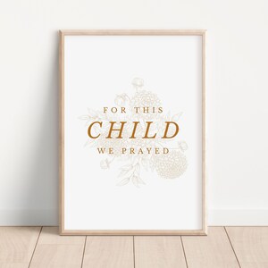 Op de afbeelding: Een witte ingelijste print met een bruin bloemenontwerp en de tekst "Voor dit kind hebben we gebeden".