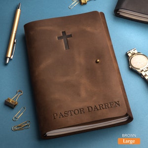 May include: A brown leather journal with a cross embossed on the front cover. The journal is personalized with the name "PASTOR DARREN".