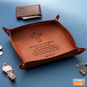 May include: A brown leather catchall tray with a cross and the text "Be strong and courageous." A brown leather wallet and a silver watch are also visible. The tray is labeled "Large".