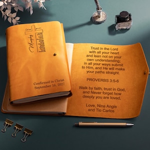 May include: A tan leather journal with a cross design and the text "Murphy" and "Confirmed in Christ September 16, 2027" on the cover. The interior flap features the text "Trust in the Lord... Proverbs 3:5-6" and a personalized message.