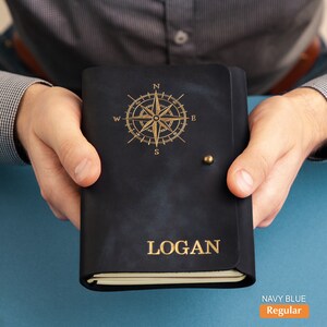 Pu&ograve; includere: Diario in pelle blu navy con un design a rosa dei venti dorata e il nome "LOGAN" impresso sulla copertina. Il diario ha una chiusura con bottone in ottone. Il testo "NAVY BLUE Regular" &egrave; nell'angolo in basso a destra.