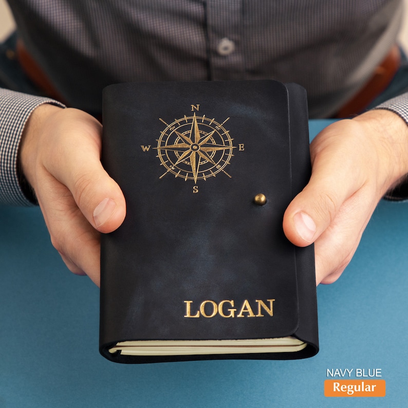 Pu&ograve; includere: Diario in pelle blu navy con un design a rosa dei venti dorata e il nome "LOGAN" impresso sulla copertina. Il diario ha una chiusura con bottone in ottone. Il testo "NAVY BLUE Regular" &egrave; nell'angolo in basso a destra.