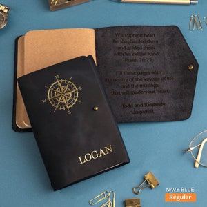 May include: A navy blue leather journal with a gold compass design and the name "LOGAN" embossed on the front. The back cover has a quote about shepherding and guiding with a skillful hand, and a message to fill the pages with the poetry of life. The quote is attributed to Psalm 78:72. The journal is labeled "NAVY BLUE Regular".