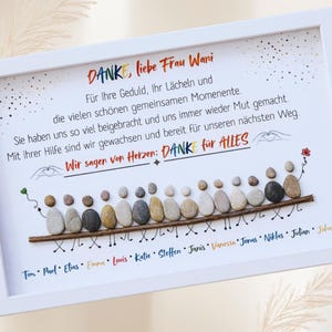 May include: A framed artwork with the words "DANKE, liebe Frau Wani" in red and black. The artwork features a line of pebble figures, each with a name below. The background is white with decorative dots.