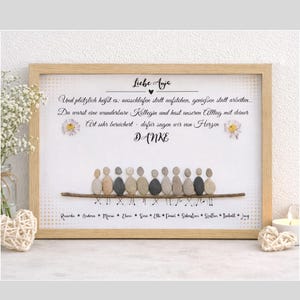 Könnte beinhalten: Ein gerahmtes Kunstwerk mit einem hellen Holzrahmen. Das Kunstwerk zeigt ein Kieselkunst-Design von Personen, die auf einem Ast sitzen, mit deutschem Text über und unter dem Bild. Der Text enthält das Wort "DANKE".