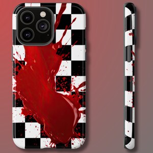 May include: A black and white chequered phone case with a red blood splatter design. The case has a raised camera bump.
