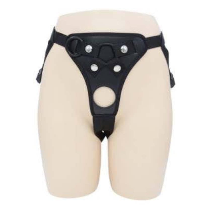 May include: Black leather harness with adjustable straps and metal buckles. The harness has a large, round opening in the front.