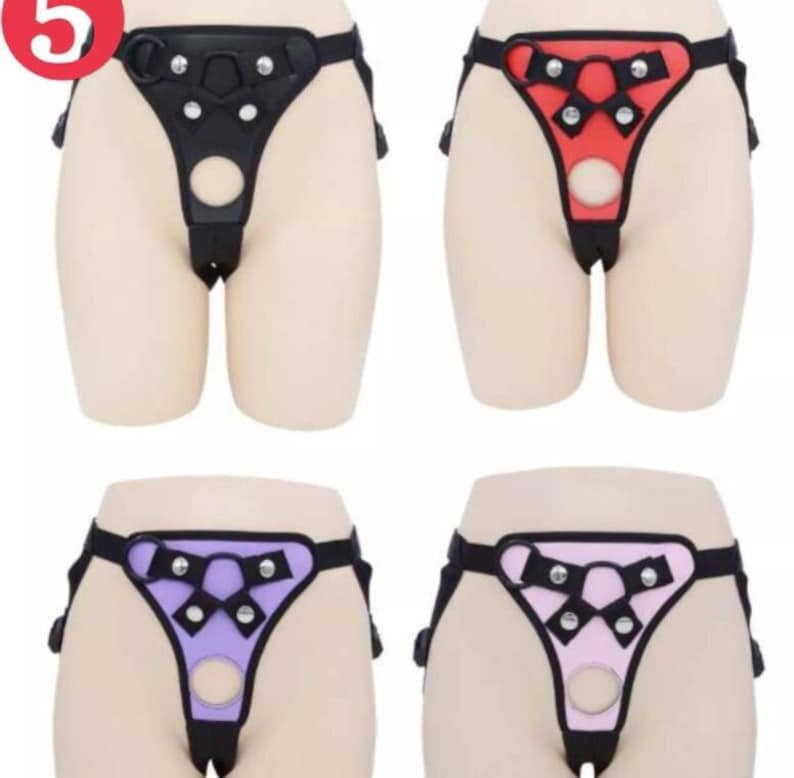 May include: Four different colored leather harnesses with adjustable straps and metal rings. The harnesses are black, red, purple, and pink.