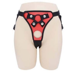 May include: A red and black leather harness with adjustable straps and metal buckles. The harness has a large, circular opening in the front.