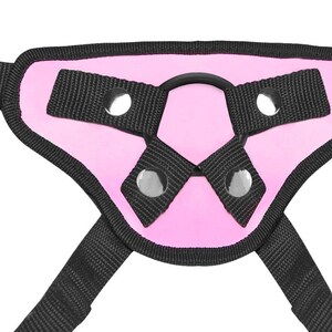 May include: Pink padded harness with black straps and metal rings. The harness has a D-ring in the center.