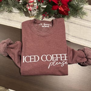 Könnte beinhalten: Ein maroonfarbener Pullover mit dem Text "ICED COFFEE please" in weißen Buchstaben. Der Pullover ist in Größe M.