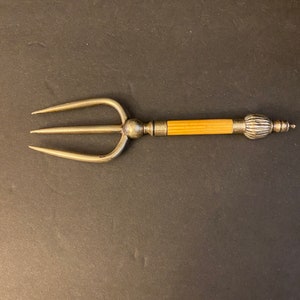 Könnte beinhalten: Eine silberne dreizackige Gabel mit einem Knochengriff. Der Griff ist hellbraun und hat einen dekorativen Knopf am Ende.