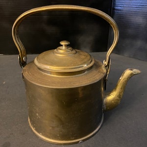 May include: A vintage brass teapot with a rounded body and a curved handle. The teapot has a lid with a knob on top and a spout on the side.