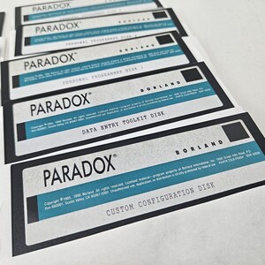 May include: A stack of five vintage 3.5-inch floppy disks for the Paradox software by Borland. Each disk features a white label with black text, a blue horizontal stripe, and specific titles including Personal Programmer, Data Entry Toolkit, and Custom Configuration.