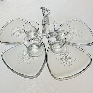 May include: A set of five clear glass serving dishes with snowflake designs. The dishes are arranged in a flower shape with a clear glass angel figurine in the center.