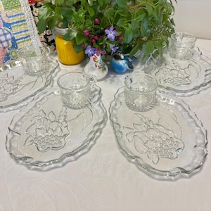Puede incluir: Juego de cuatro platos de aperitivo de vidrio transparente con tazas a juego. Cada plato presenta un diseño en relieve de una cesta de frutas con uvas y hojas.