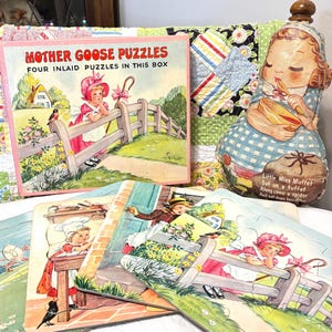 May include: Vintage "Mother Goose Puzzles" box set with four inlaid puzzles. The box is pink and features a girl in a pink dress leaning on a fence. The puzzles depict scenes from nursery rhymes. A fabric doll of Little Miss Muffet is also visible.