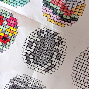 May include: A selection of pixel art designs, each in a mosaic style. The designs include a green square, a colourful burger, and other geometric shapes. The artwork is created with a grid of small squares, filled with various colours.