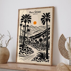 Pode incluir: Uma ilustra&ccedil;&atilde;o em preto e branco de palmeiras e um rio sinuoso em uma paisagem des&eacute;rtica. O texto "Palm Springs, CAHUILLA" est&aacute; no topo da imagem.