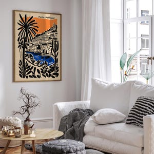May include: A framed art print depicting a coastal scene in Porto, Portugal. The artwork features a stylized illustration with a beige background, an orange sky, and black and blue elements. The print is displayed in a living room setting.