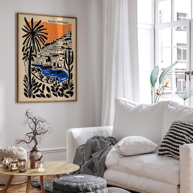 May include: A framed art print depicting a coastal scene in Porto, Portugal. The artwork features a stylized illustration with a beige background, an orange sky, and black and blue elements. The print is displayed in a living room setting.