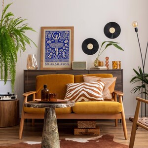 May include: A mustard yellow velvet sofa with a zebra print throw pillow and two solid brown throw pillows. The sofa is in a living room with a vintage record player, a framed print of a ballerina, and a potted plant.