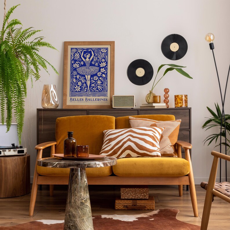 May include: A mustard yellow velvet sofa with a zebra print throw pillow and two solid brown throw pillows. The sofa is in a living room with a vintage record player, a framed print of a ballerina, and a potted plant.