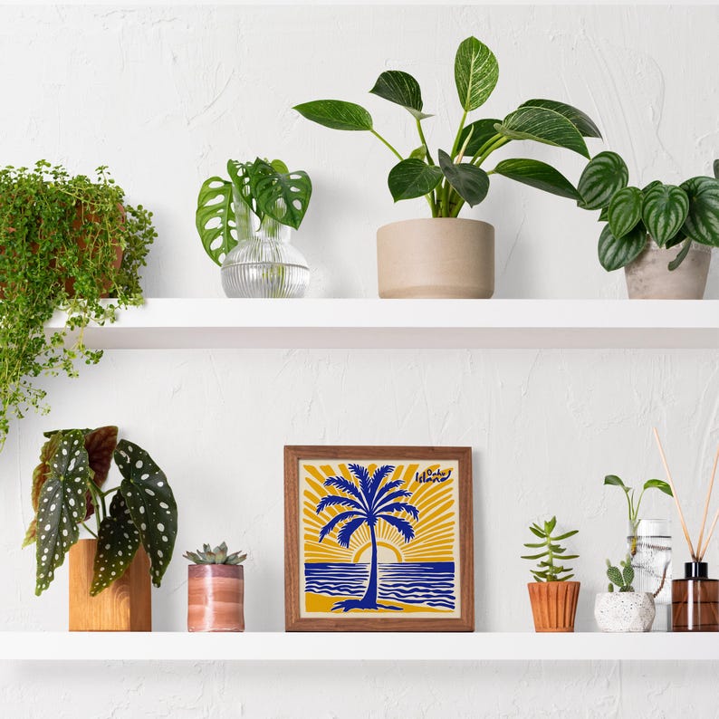 May include: A white shelf with a framed print of a blue palm tree with a yellow sunset behind it. The print has the words 'Island Vibes' at the top. The shelf is decorated with various plants in pots, including a green plant in a clear glass vase, a green plant in a brown pot, a green plant in a white pot, and a green plant in a brown pot.