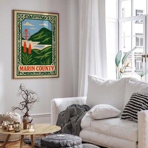 May include: A framed print of Marin County. The artwork shows a stylized Golden Gate Bridge, green hills, and blue skies. The print is in a wooden frame and is hanging on a white wall.