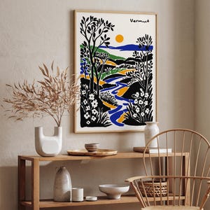 May include: A black and white illustration of a landscape with a river winding through it. The illustration is framed and hanging on a wall above a wooden shelf with various decorative items.