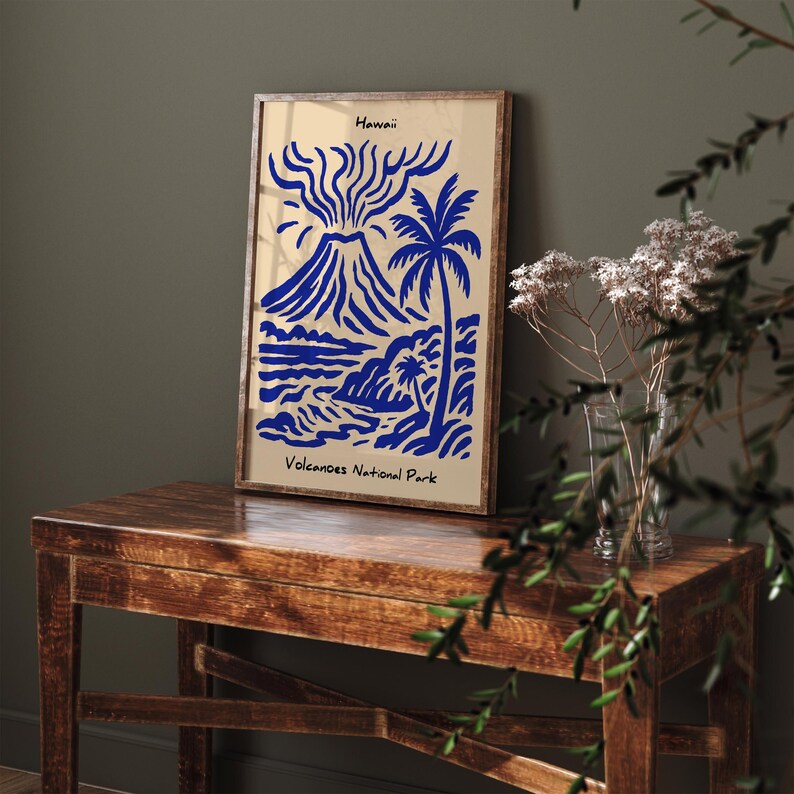 Puede incluir: Un estampado art&iacute;stico enmarcado con una ilustraci&oacute;n azul de un volc&aacute;n, palmeras y olas del oc&eacute;ano sobre un fondo beige. El estampado est&aacute; etiquetado como "Hawaii" y "Volcanoes National Park". El marco es de color marr&oacute;n oscuro.