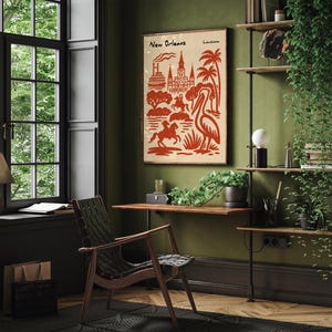Op de afbeelding: Een ingelijste poster met een vintage ontwerp met de tekst "New Orleans" en "Louisiana" in een rood-beige kleurenschema. Het kunstwerk toont iconische stadselementen, waaronder gebouwen, bomen en een pelikaan. De poster wordt weergegeven in een kamer met een houten bureau en stoel.