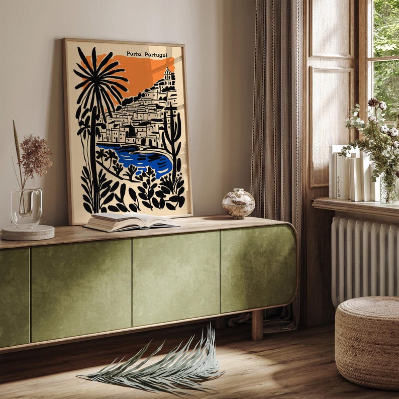 May include: A framed art print featuring a stylized illustration of Porto, Portugal. The artwork showcases a cityscape with a blue body of water, set against an orange and beige background. Black palm trees and foliage frame the scene. The text "Porto, Portugal" is at the top.