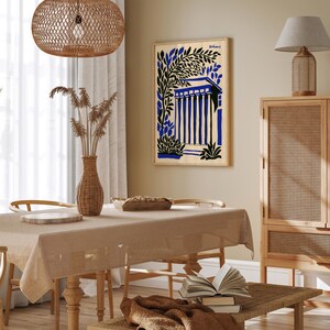 May include: A framed art print with a blue and black illustration of a building with columns and trees. The print is titled "Behrani" and is hanging on a beige wall in a room with a wooden table and chairs.