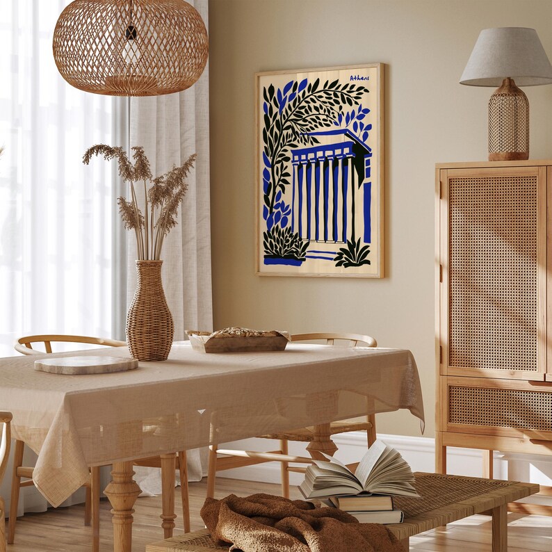 May include: A framed art print with a blue and black illustration of a building with columns and trees. The print is titled "Behrani" and is hanging on a beige wall in a room with a wooden table and chairs.